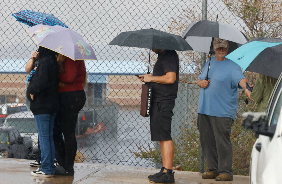 Fans hold umbrellas to protect themselves from heavy rain as they line up to attend a high scho ...