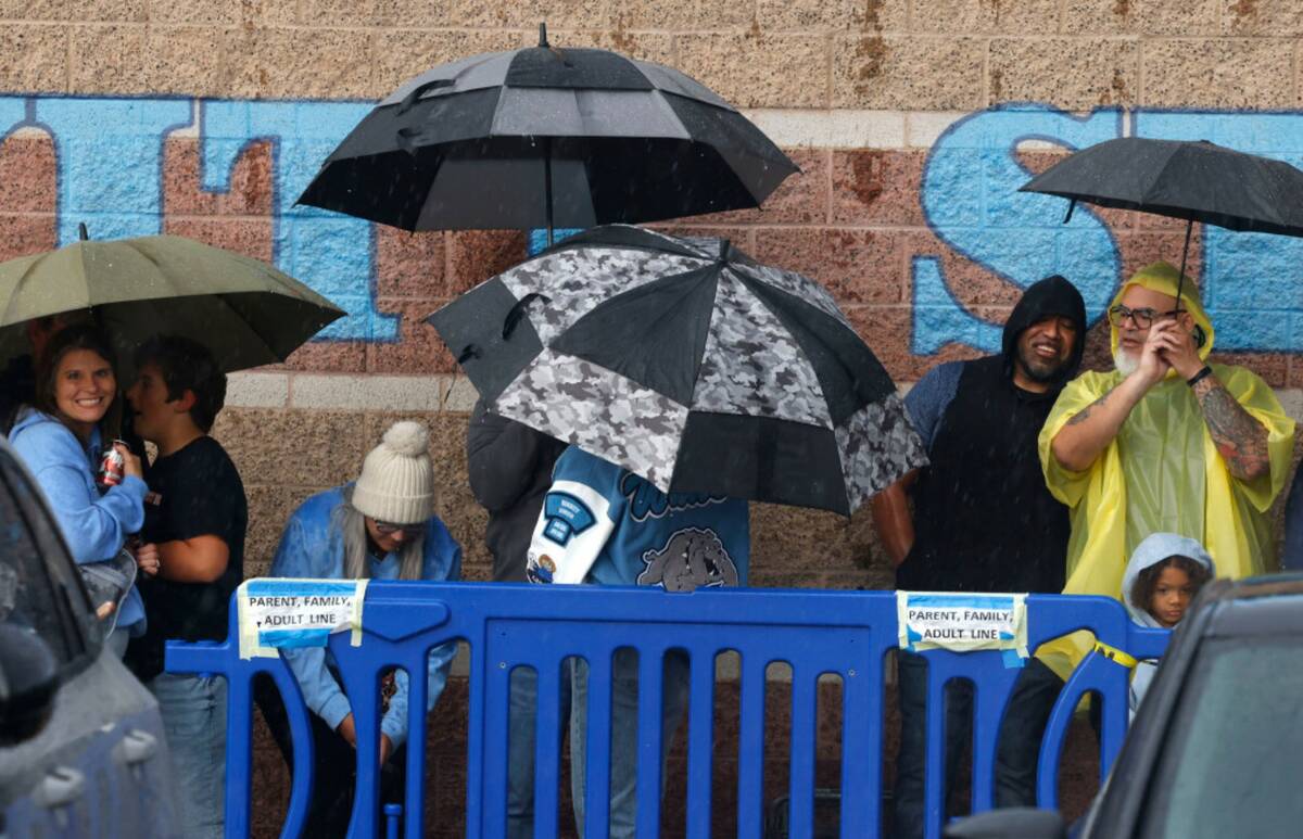Fans hold umbrellas to protect themselves from heavy rain as they line up to attend a high scho ...