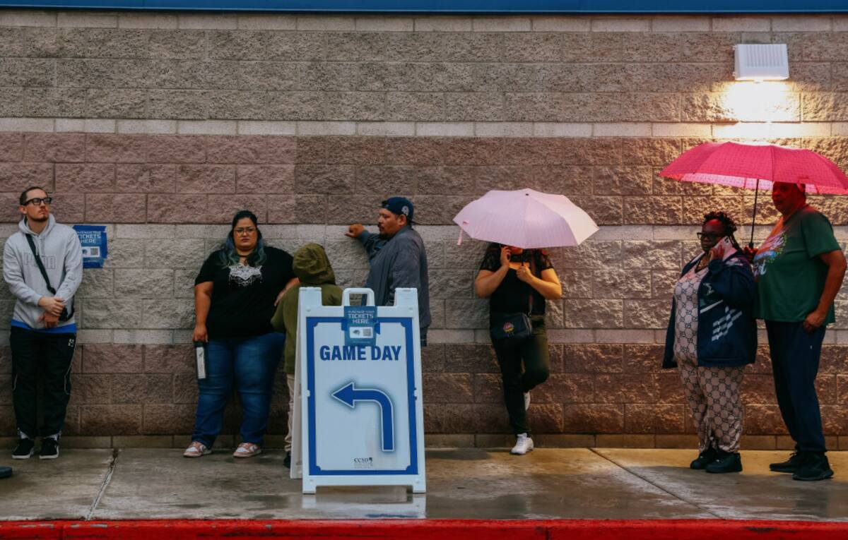Fans stand in line, some under cover of umbrellas, to enter the stadium for a football game bet ...