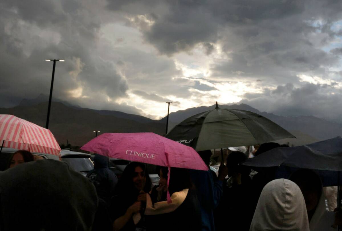 Fans hold umbrellas to protect themselves from heavy rain as they line up to attend a high scho ...