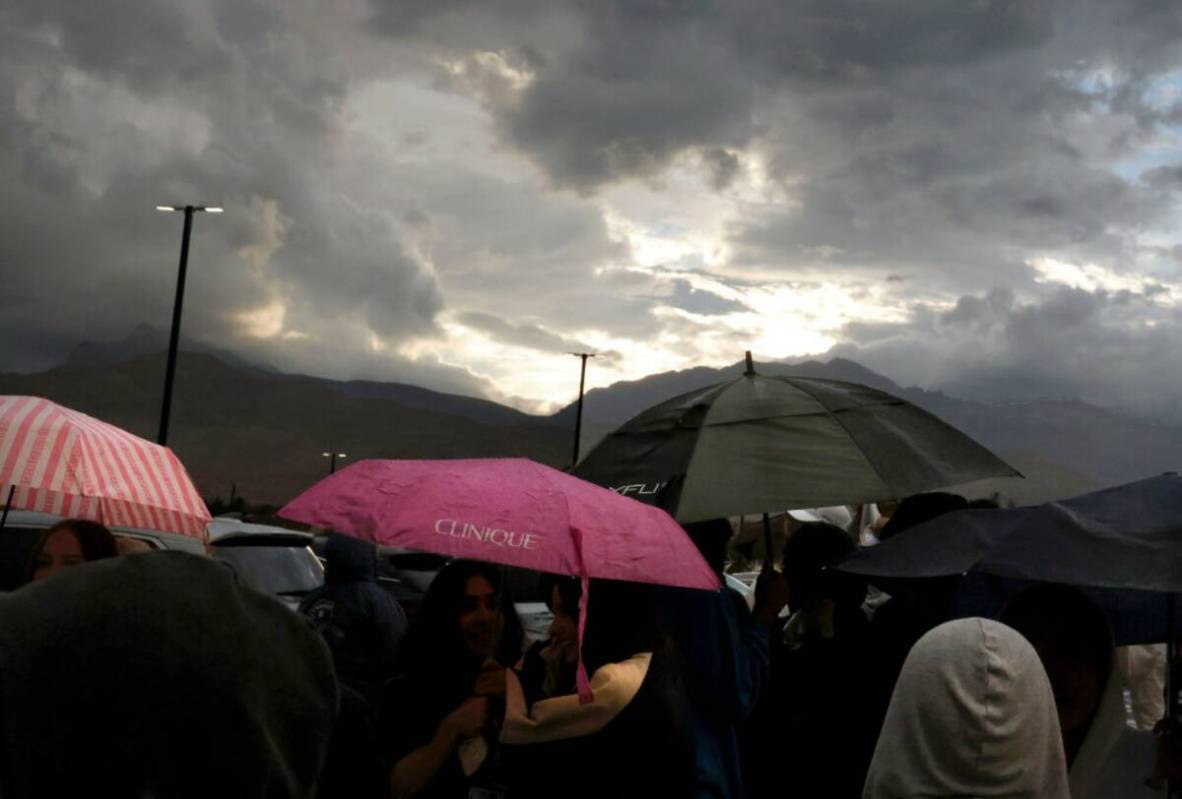 Fans hold umbrellas to protect themselves from heavy rain as they line up to attend a high scho ...