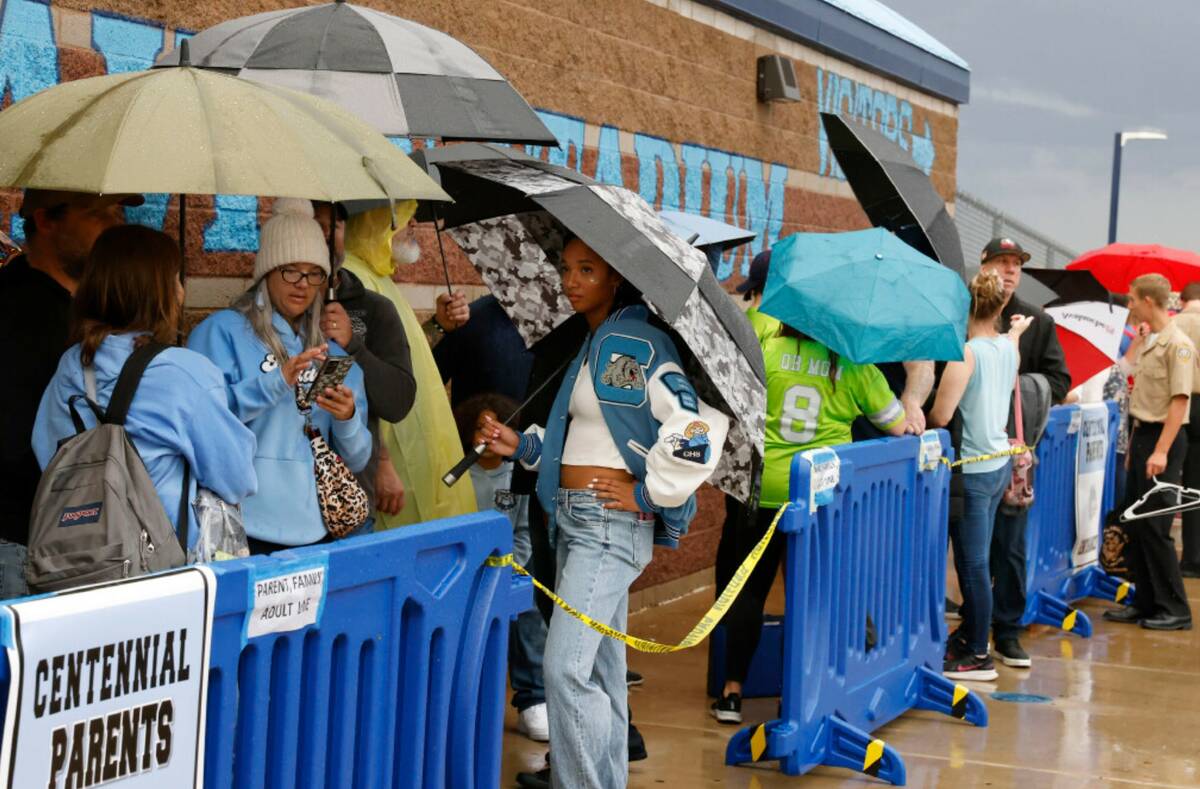 Fans hold umbrellas to protect themselves from heavy rain as they line up to attend a high scho ...