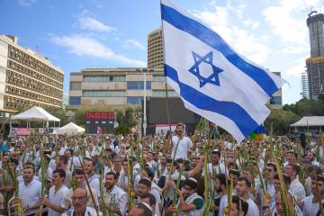 Covered in prayer shawls, men dance and hold the four items used as a symbol on the Jewish holi ...