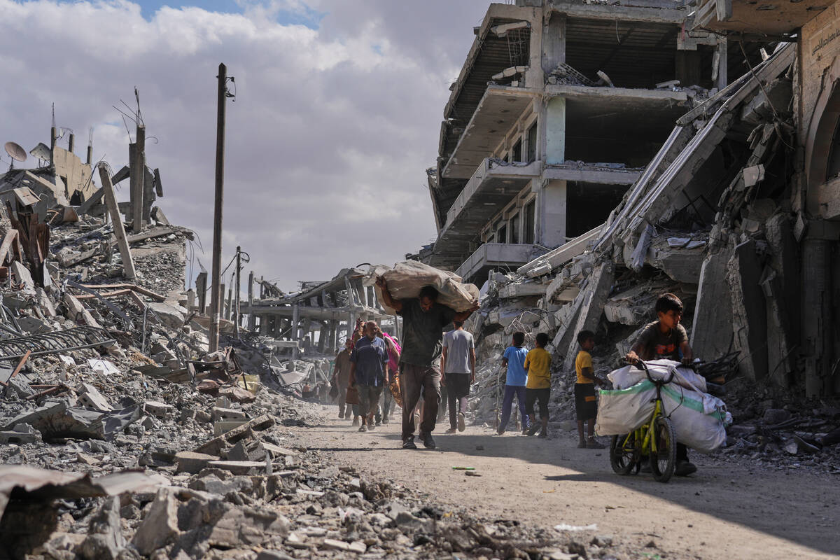 Displaced Palestinians walk with their belongings past destroyed buildings as they return to th ...