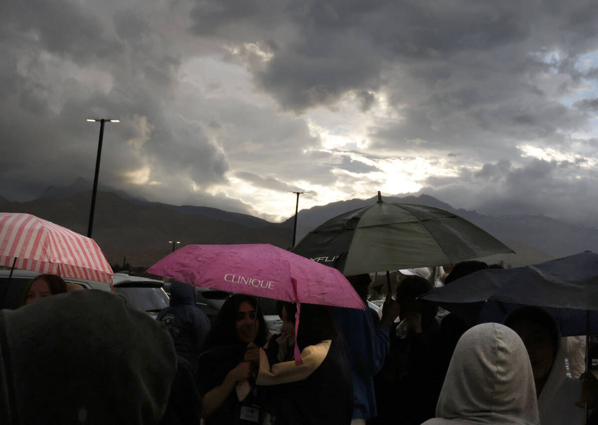 Fans hold umbrellas to protect themselves from heavy rain as they line up to attend a high scho ...