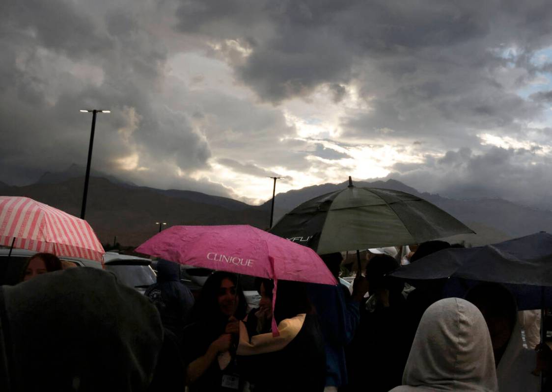 Fans hold umbrellas to protect themselves from heavy rain as they line up to attend a high scho ...