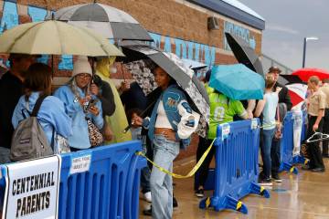 Fans hold umbrellas to protect themselves from heavy rain as they line up to attend a high scho ...