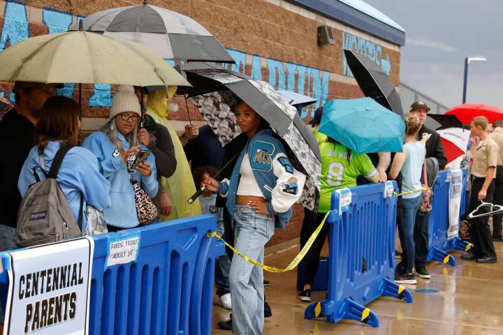 Fans hold umbrellas to protect themselves from heavy rain as they line up to attend a high scho ...