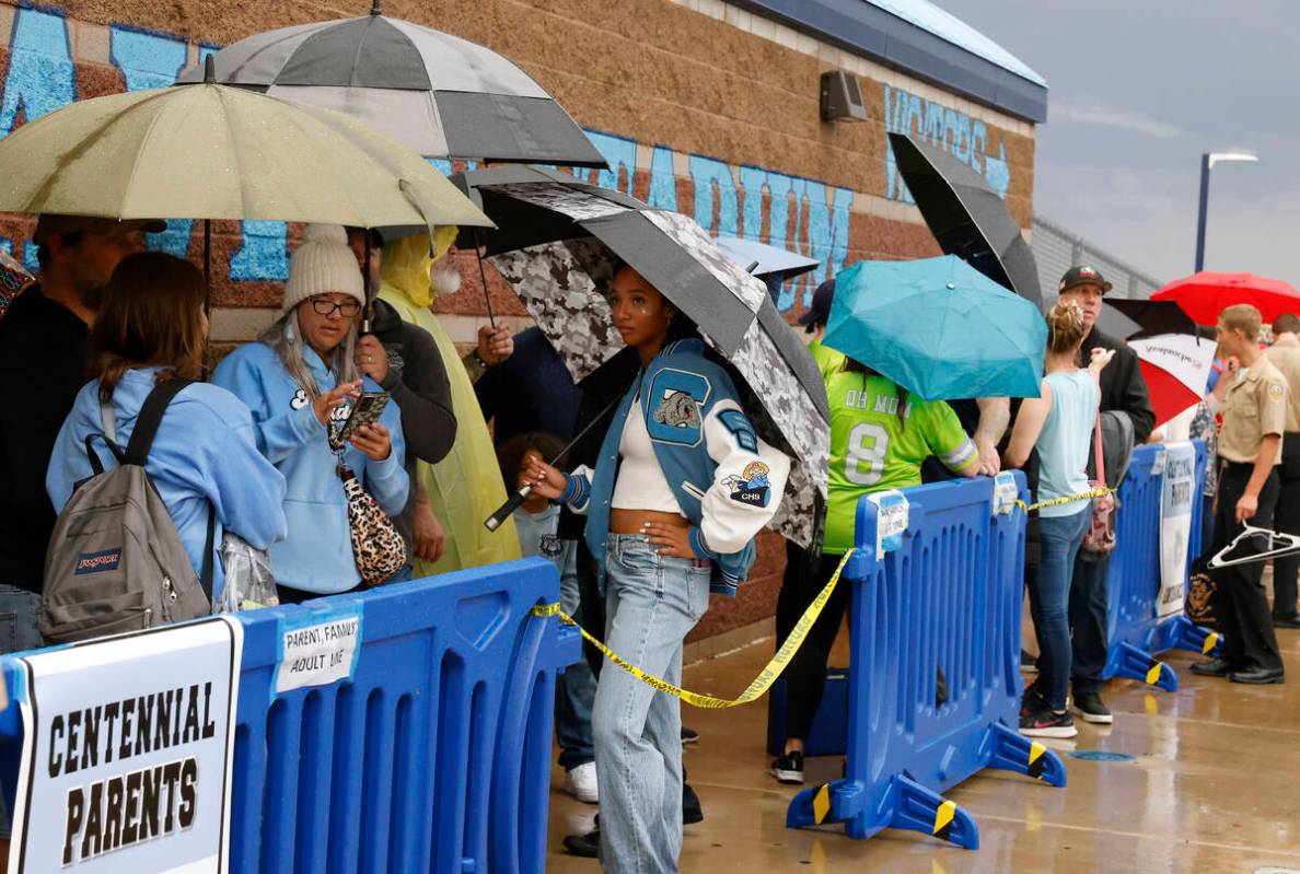 Fans hold umbrellas to protect themselves from heavy rain as they line up to attend a high scho ...