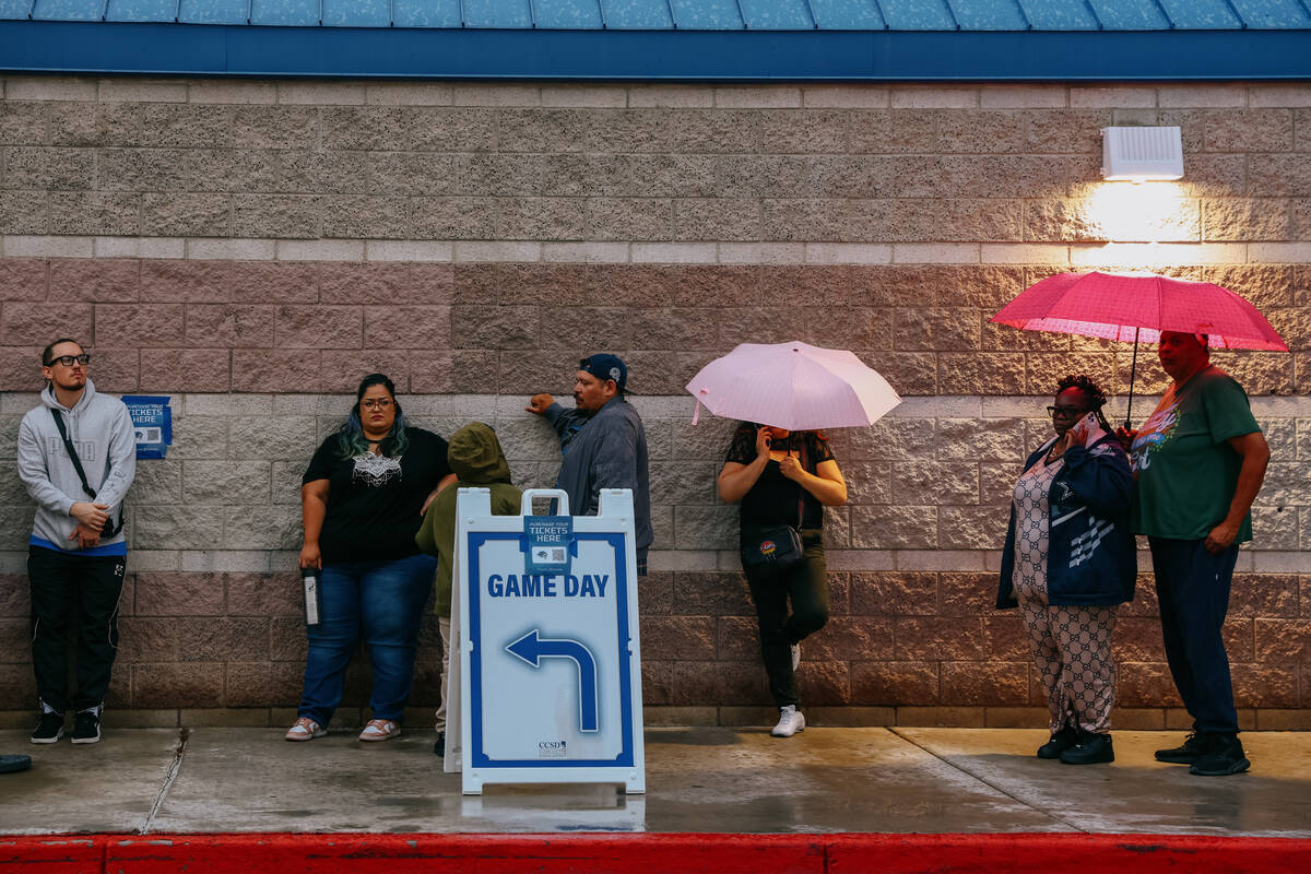 Fans stand in line, some under cover of umbrellas, to enter the stadium for a football game bet ...