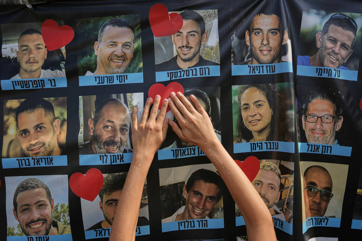 Hands paste a heart-shaped sticker onto a banner with pictures of Israeli hostages during a a g ...