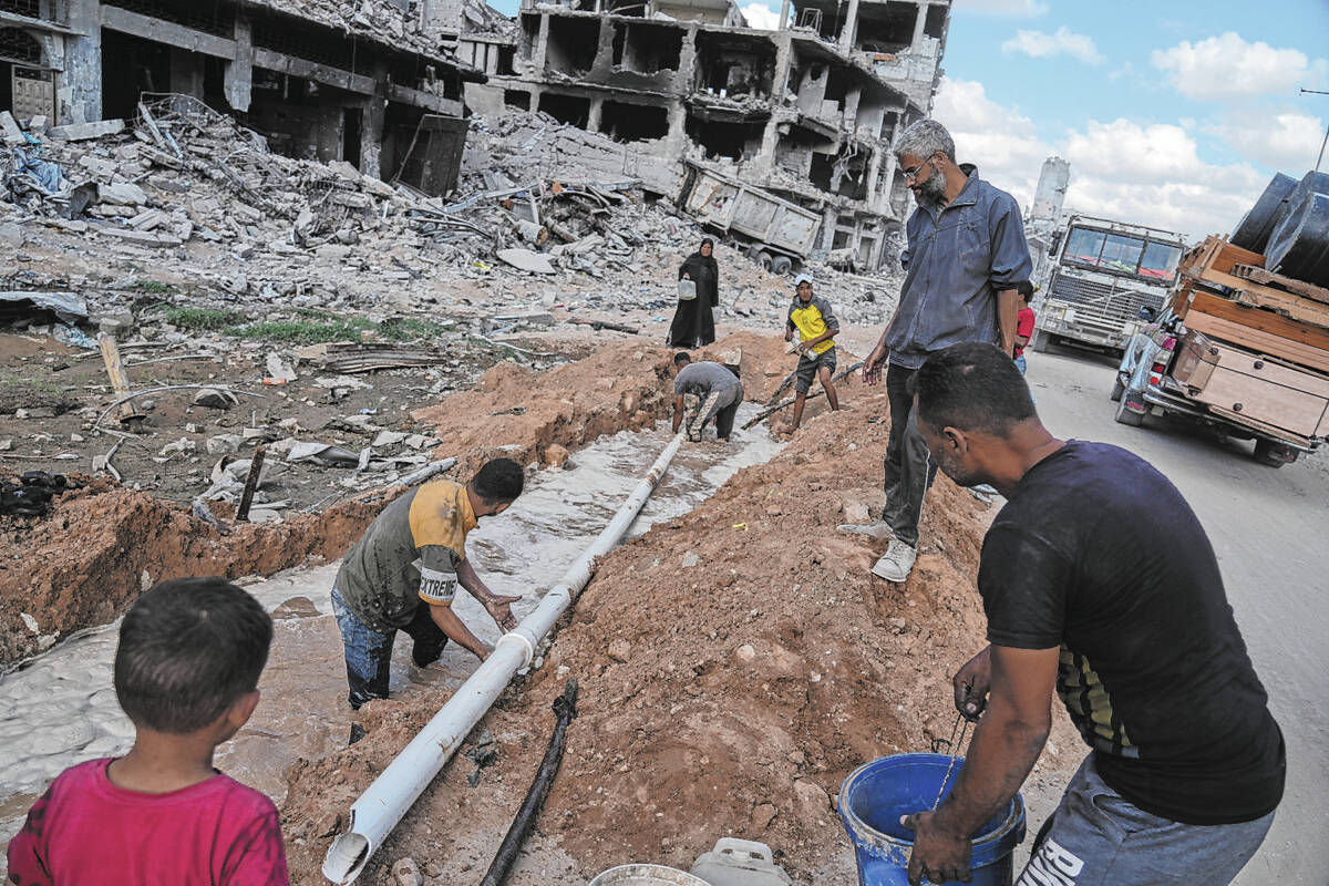 Palestinians repair a water pipe amid destroyed buildings in Gaza City, Sunday, Oct. 12, 2025, ...