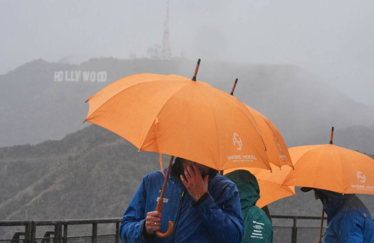 Tourists from Poland carry umbrellas in front of the Hollywood sign as rain falls while visitin ...