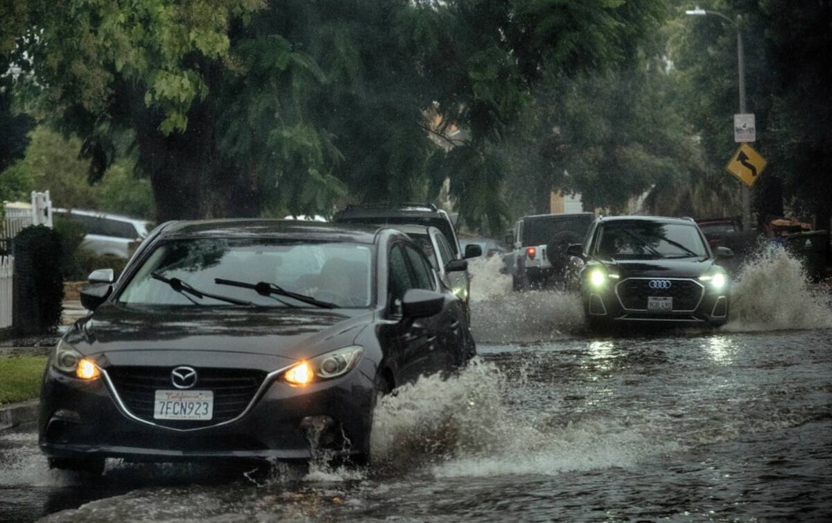 Morning commuters maneuver a flooded street during a flash flood warning in the San Fernando Va ...