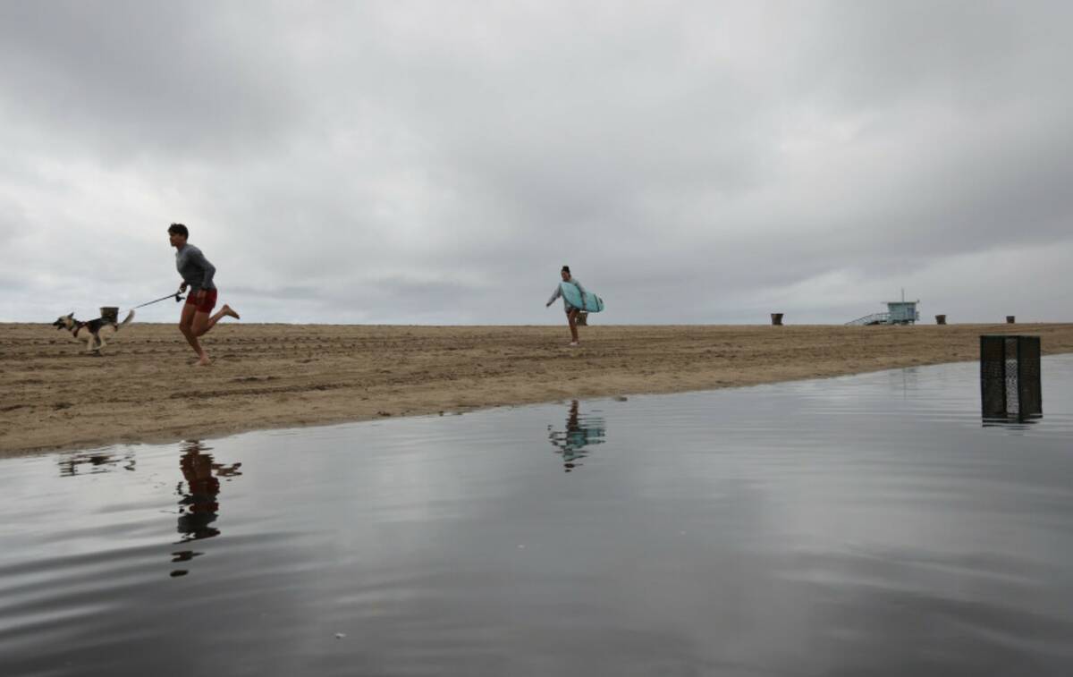 People run on a beach along a flooded path after heavy rains Tuesday, Oct. 14, 2025, in Santa M ...