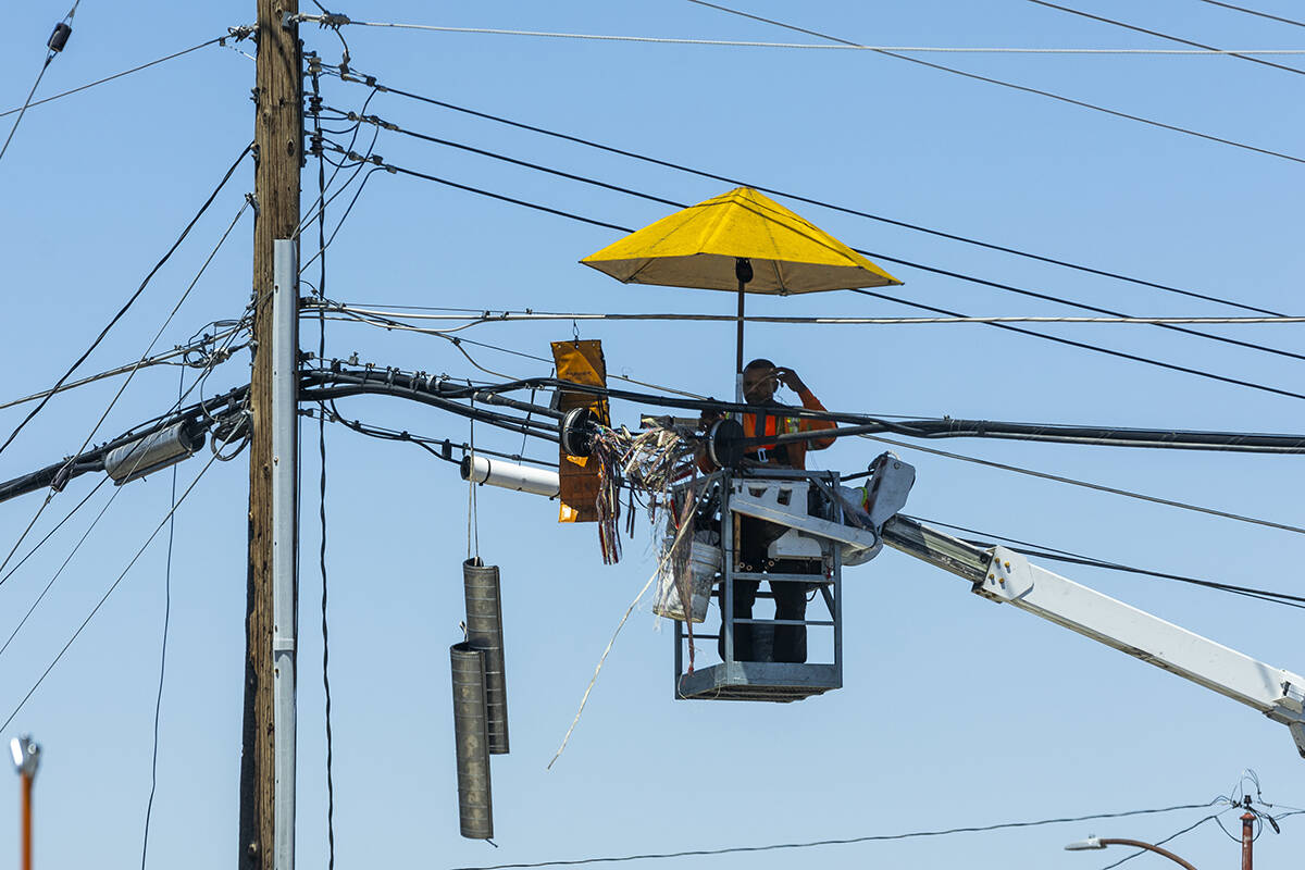 A lineman works beneath an umbrella along West Owens Avenue as the weather heats up on Friday, ...