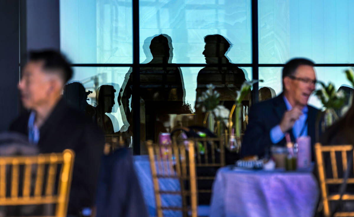 Invited guests are reflected in patio windows as they and others chat during the Vegas Tech Sum ...