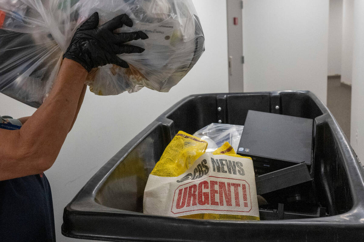 A cleaning person throws a bag of trash in a dumpster as members of the media pack up their bel ...