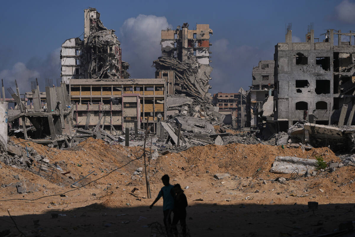 Palestinians walk through the destruction caused by the Israeli air and ground offensive in the ...