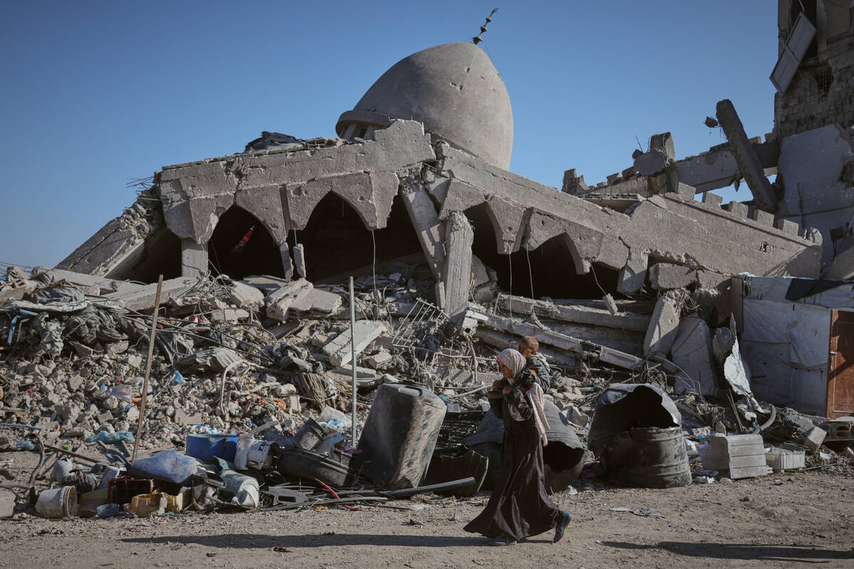 A Palestinian woman carrying her child walks past a destroyed mosque in Gaza City Sunday, Oct. ...