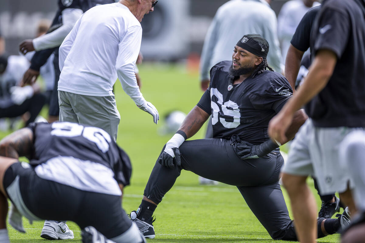 Raiders head coach Pete Carroll chats with a defensive tackle Adam Butler (69) as they stretch ...