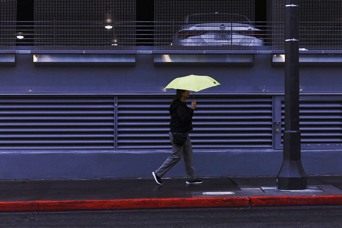 A woman carries an umbrella for protection from morning rain showers while walking in downtown ...