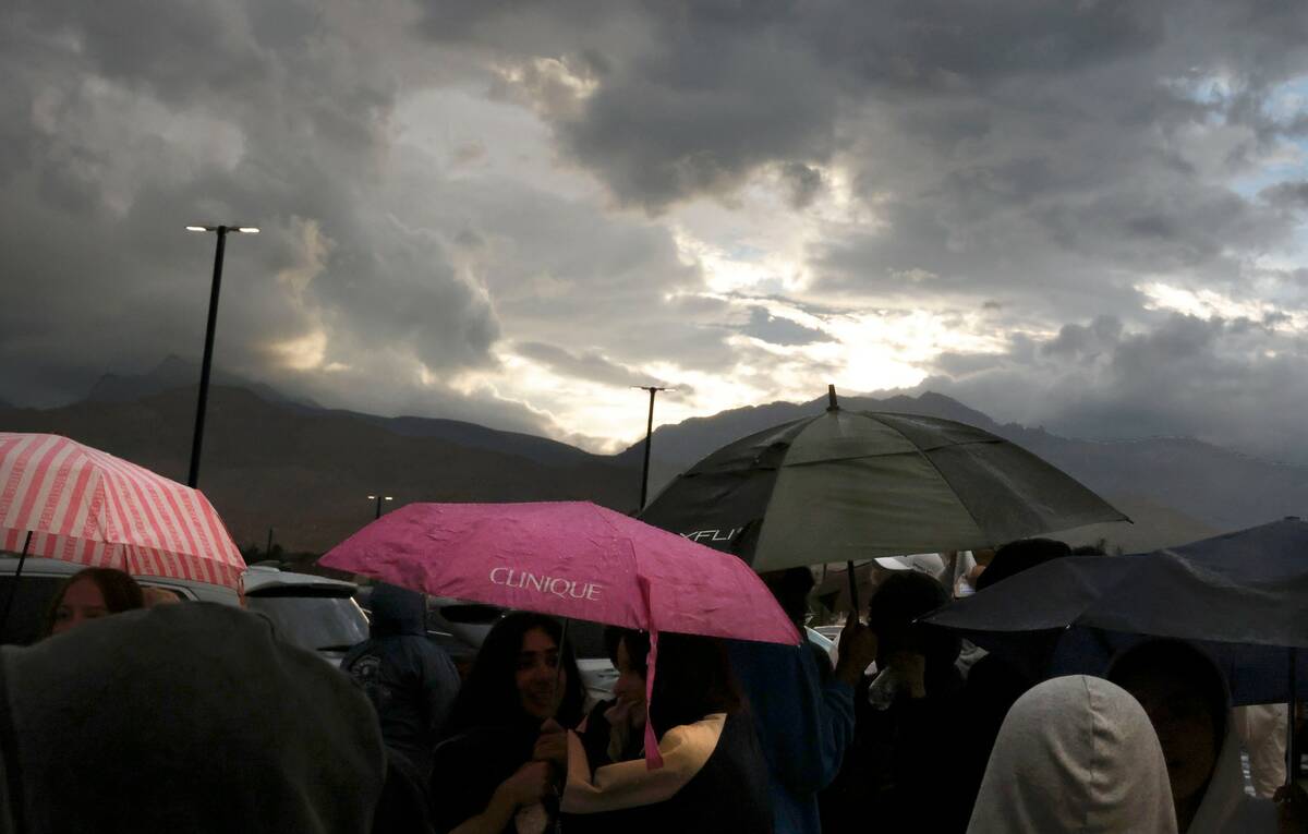 Fans hold umbrellas to protect themselves from heavy rain as they line up to attend a high scho ...