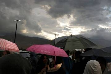 Fans hold umbrellas to protect themselves from heavy rain as they line up to attend a high scho ...
