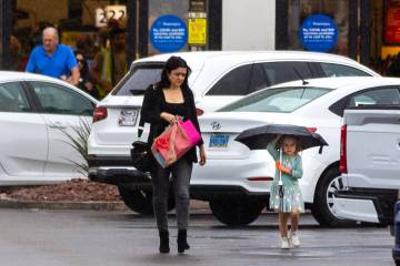 A child stays dry under an umbrella as she and a woman leave a Smiths grocery store while rain ...