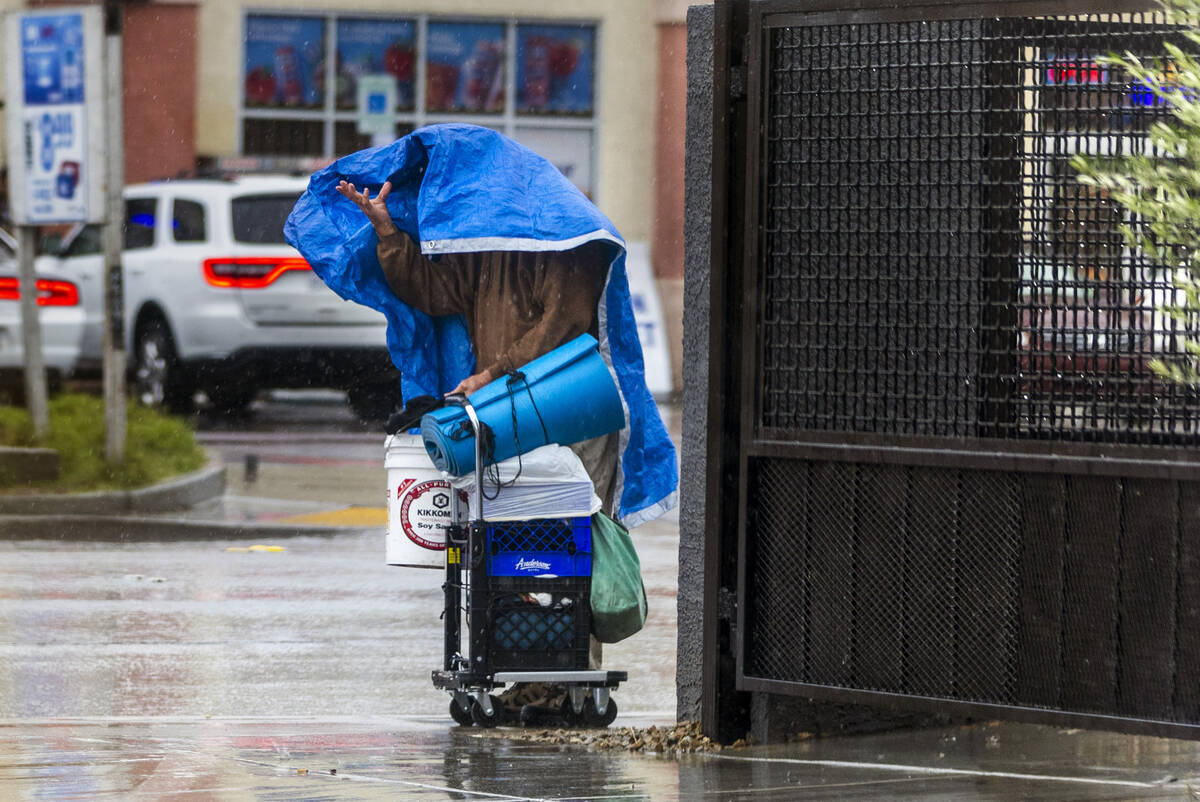 A man checks from under his tarp to see if the rain is still coming down along East Twain Avenu ...