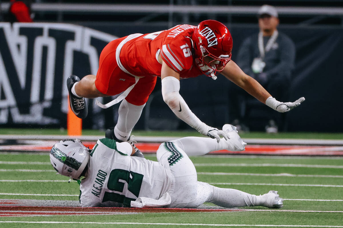 UNLV linebacker Blesyng Alualu-Tuiolemotu (15) leaps over Hawaii quarterback Micah Alejado (12) ...