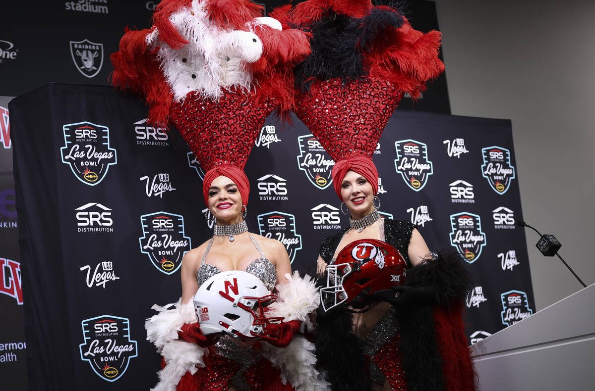 Showgirls Porsha Revesz, left, and Jenn Autry pose with football helmets from Nebraska and Utah ...