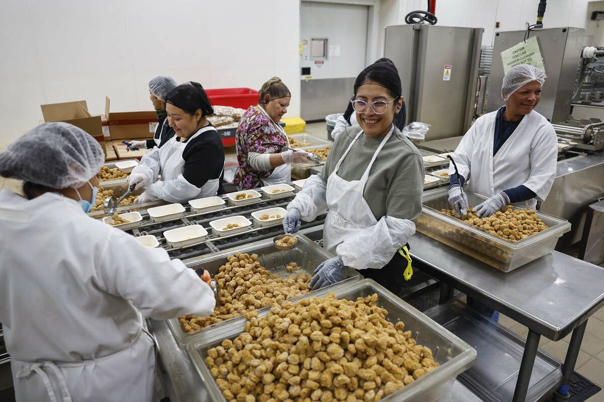 Food service workers add tater tots to trays on assembly lines at CCSD’s Central Kitchen ...