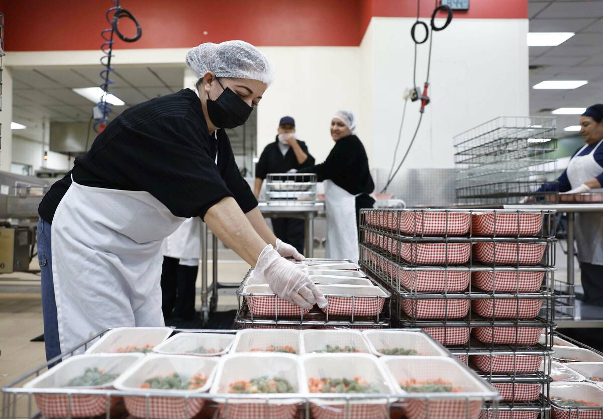 Food service workers pull completed trays off assembly lines at CCSD’s Central Kitchen T ...