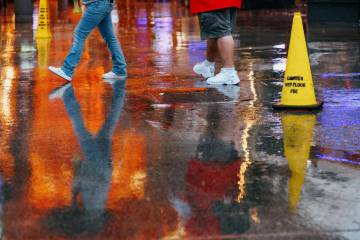 Pedestrians walk past a cone cautioning wet floors on Tuesday, Nov. 18, 2025 at the Fremont Str ...