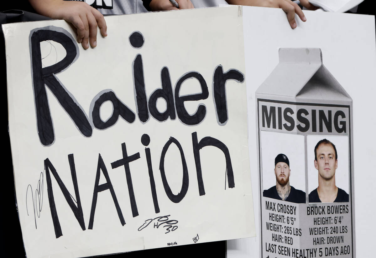 Fans hold signs with photographs of injured Raiders defensive end Maxx Crosby (98) and tight en ...