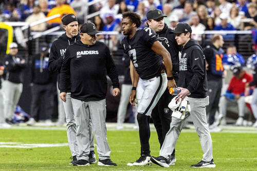 Raiders quarterback Geno Smith (7) is helped off of the field by trainers and guard Jackson Pow ...