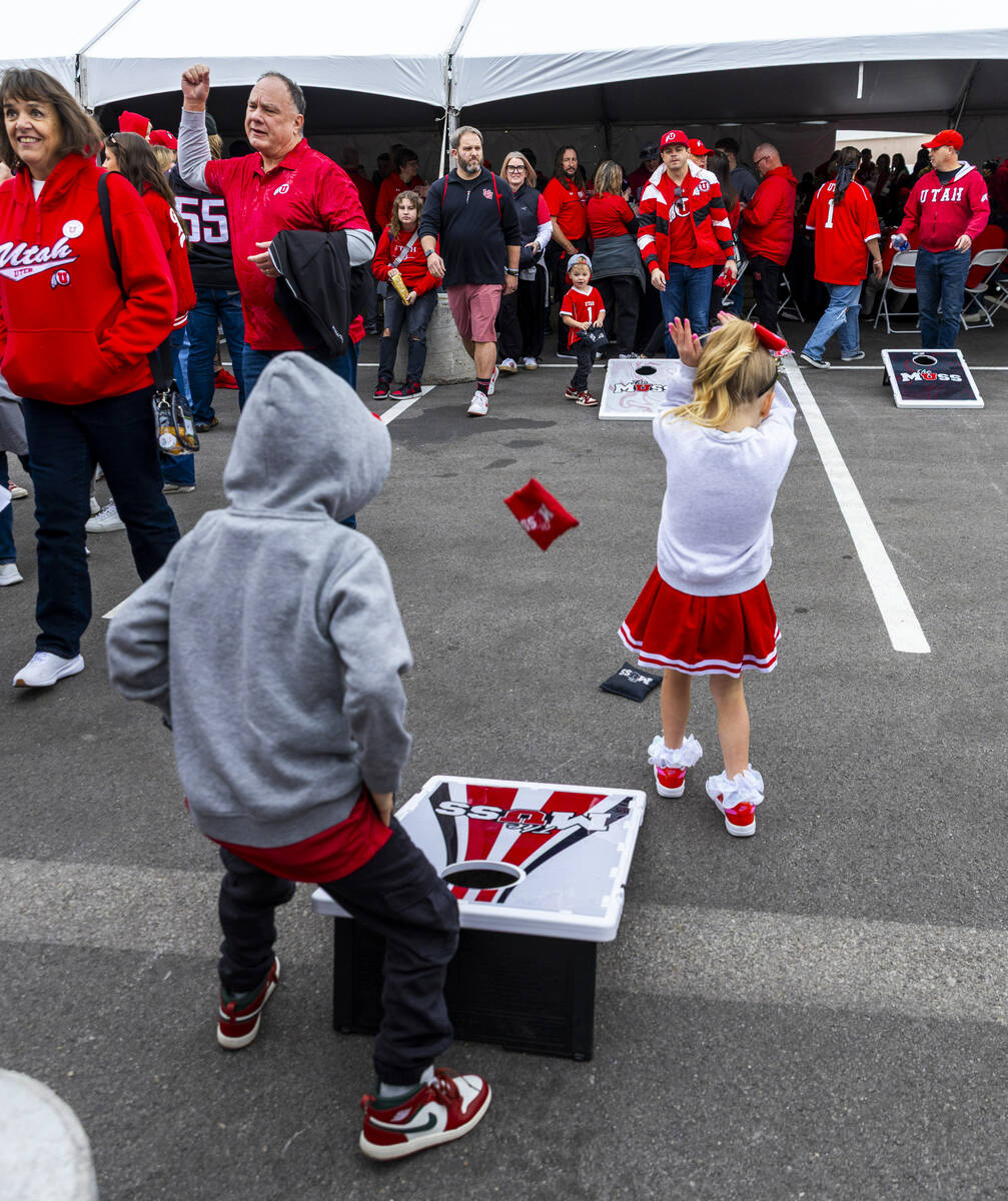 A young Utah tailgater covers up from an incoming beanbag as fans play corn hole while enjoying ...