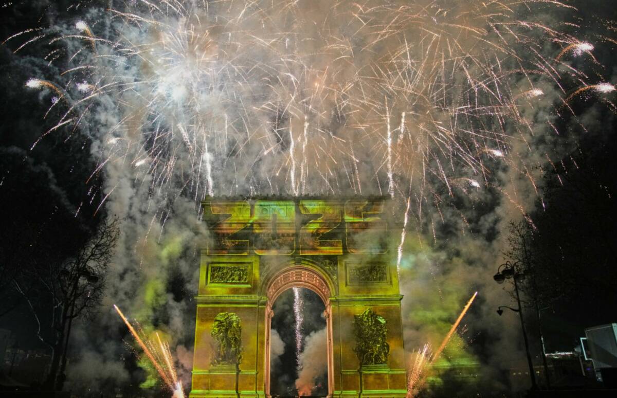 A light show is projected on the Arc de Triomphe as fireworks explode during New Year celebrati ...