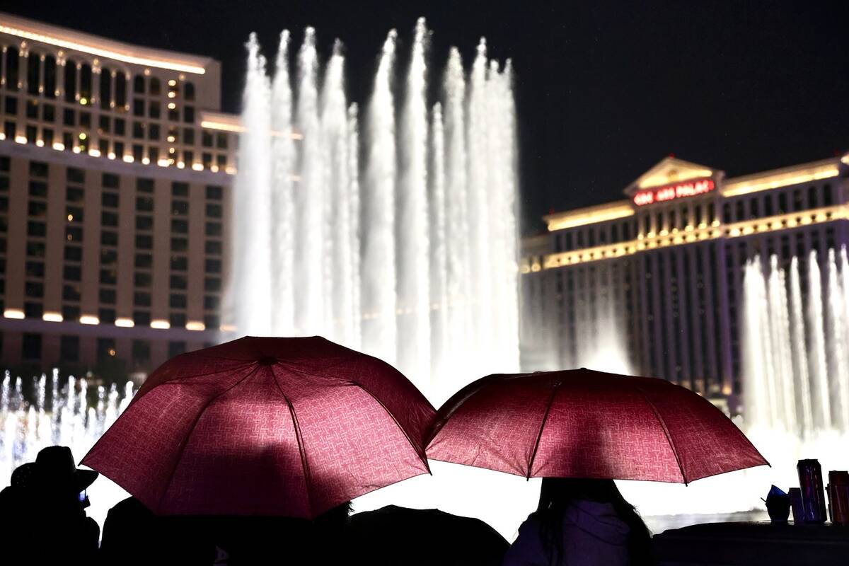 People brave light rain to watch the Bellagio fountain show on the Las Vegas Strip on Dec. 31, ...