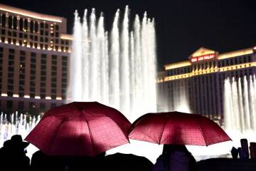 People brave light rain to watch the Bellagio fountain show on the Las Vegas Strip on Dec. 31, ...