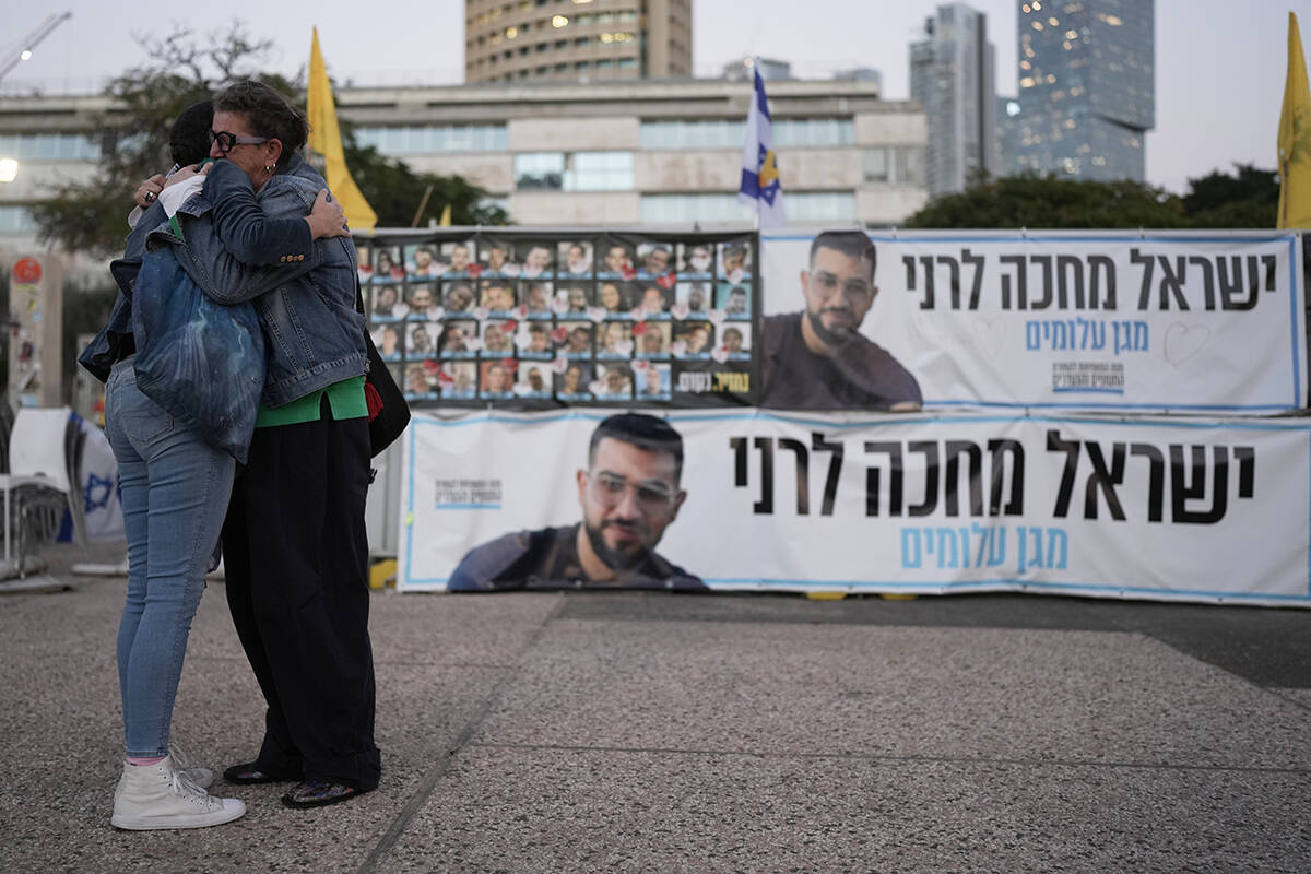 Two women embrace next to a banner with a photo of Ran Gvili after the announcement that the ho ...