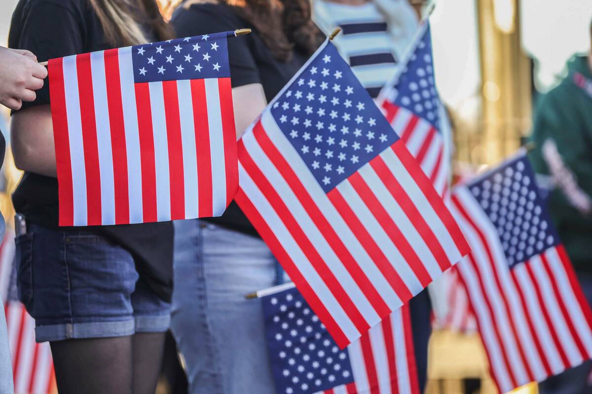 Attendees hold American flags while listening to remarks before a semi-truck carrying approxima ...
