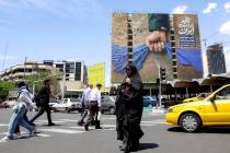 A woman crosses a street near a billboard on the facade of a building depicting the Strait of H ...