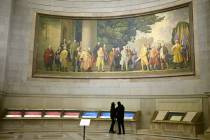 Two visitors look at exhibits beneath a large wall mural showing the signing of the Declaration ...