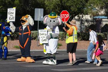 Crossing guard Todd Gainley helps pedestrians cross the street as local sports team mascots hol ...