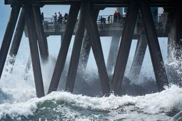 People walk on a pier as large waves from Hurricane Marie break on the shore, Monday, Sept. 7, ...