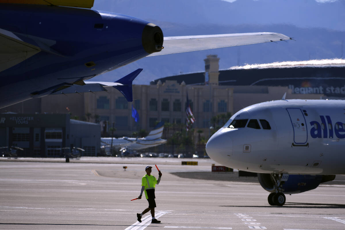 A ground crew worker guides an Allegiant jet across the tarmac at Harry Reid International Airport, with the Las Vegas Valley mountains in the background
