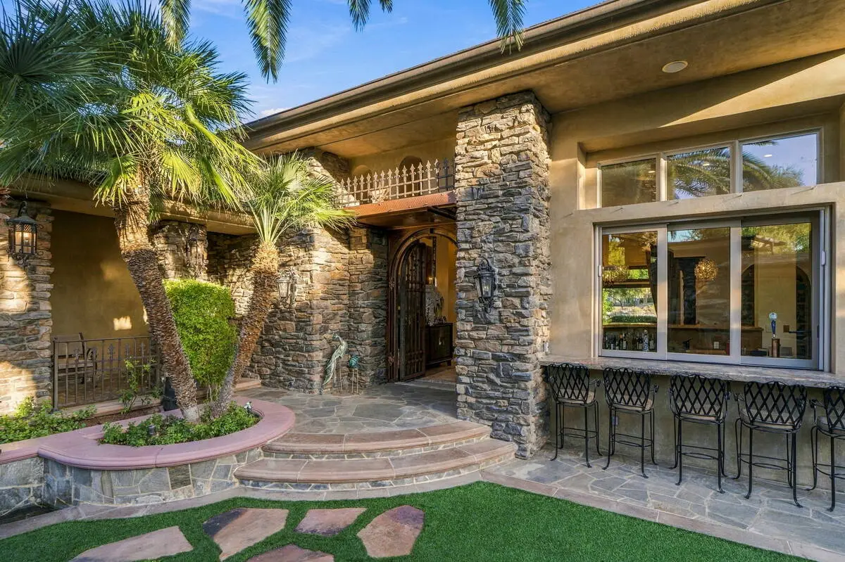 Stone entry courtyard with palm trees, a carved wooden front door, and outdoor bar seating at the MacDonald Highlands home on Foothills Village Drive