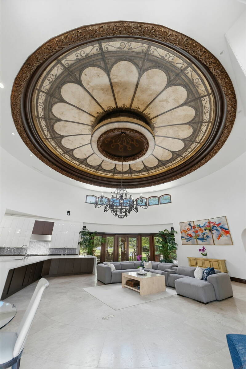 Great room with a large ornate domed ceiling, gray sectional sofas, and tall windows inside the Foothills Village Drive home in Henderson